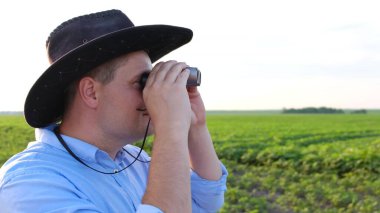 Neşeli tarım uzmanı soya fasulyesi tarlasına dürbünle bakıyor..