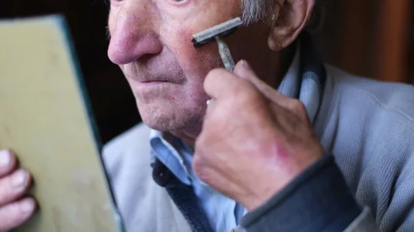 Um homem idoso rapa a cara à frente de um espelho. O pensionista rapa a barba.. — Fotografia de Stock