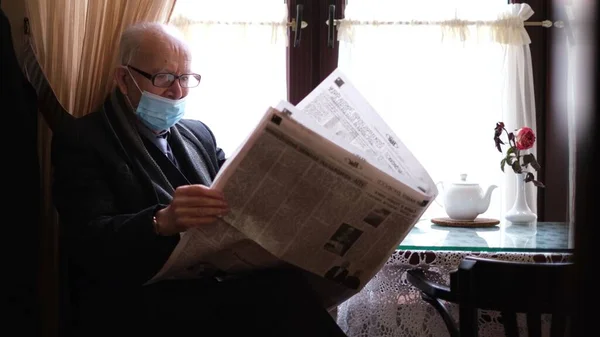 Um homem aposentado com uma máscara senta-se em um café e lê um jornal. — Fotografia de Stock