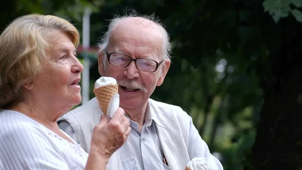 Couple de personnes âgées mangeant de la glace sur un banc de parc. Concept d'amour — Photo