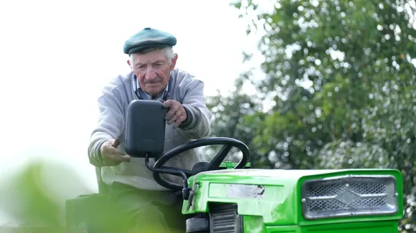 Hombre retirado en su mini-tractor. Un trabajador del pueblo trabaja en su campo —  Fotos de Stock