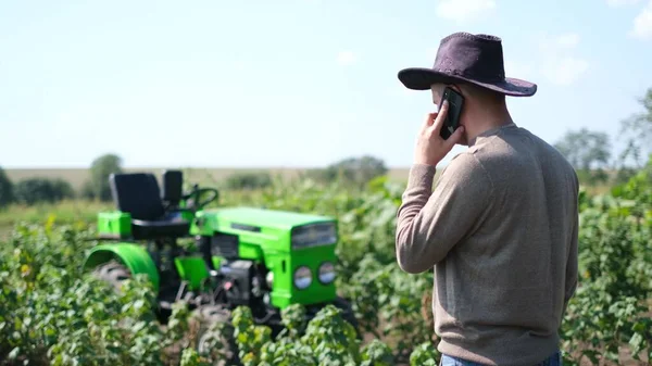 젊은 농부가 스마트폰을 사용하고 있는데, 트랙터 근처에서 쉬고 있습니다. — 스톡 사진