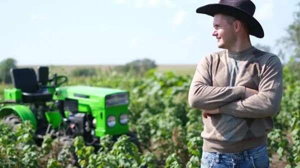 若い幸せな農家は彼の新しいトラクターで喜びます。緑のミニトラクターの近くのフィールド上の男. — ストック写真