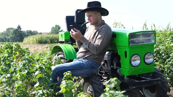 한 젊은 농부가 트랙터 근처에서 일하는 동안 스마트폰을 들고 있다. — 스톡 사진