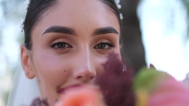 Hermosa novia sosteniendo un ramo de cerca y mirando en el marco. — Vídeo de stock