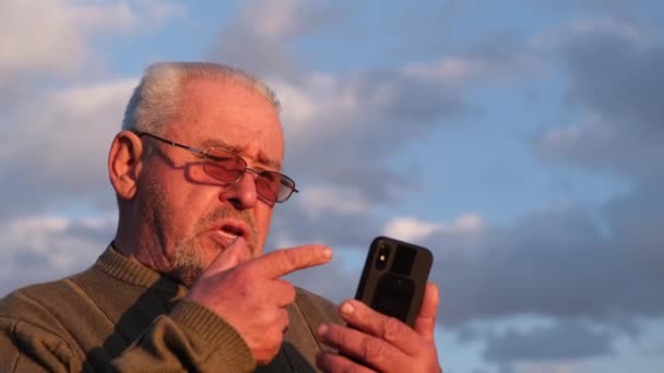 공원 벤치에 앉아 스마트폰을 보고 있는 노인 회색 머리 남자 — 비디오