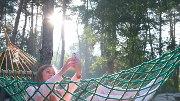 Menina jovem tirando foto selfie no celular enquanto deitado na rede. — Vídeo de Stock