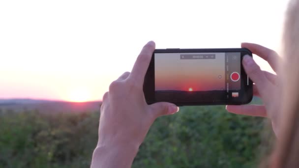 Uma menina capturar o belo momento do pôr do sol com seu smartphone. Silhueta viajante solo. — Vídeo de Stock