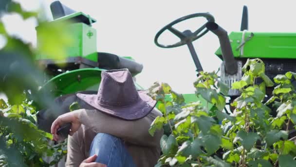 Ein Landwirt ruht neben einem Traktor auf einem Feld. — Stockvideo