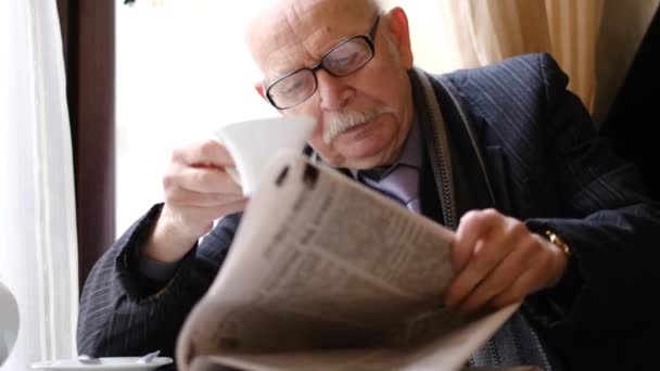 An elderly man reads a newspaper at a table in a cafe. — 图库视频影像