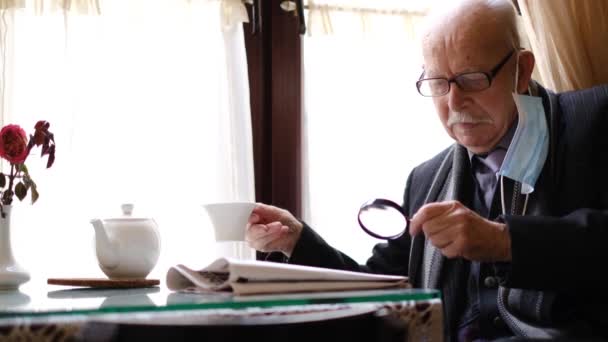 Senior man met een kop koffie leest een krant door een vergrootglas. — Stockvideo