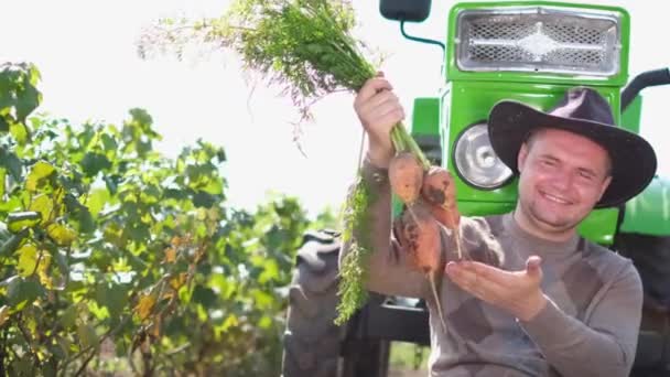 Χαρούμενος αγρότης με καρότο σε χωράφι κοντά στο τρακτέρ του — Αρχείο Βίντεο