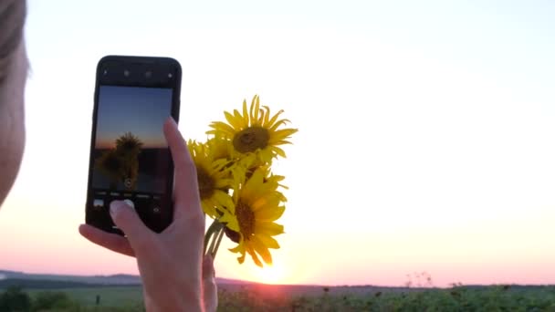 Dívka fotí květiny na smartphonu při západu slunce. 