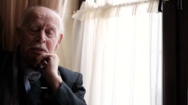 Yaşlı, kır saçlı bir dede pencerede oturuyor.