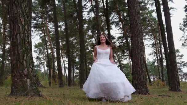 Happy smiling bride runs through the woods holding a dress in her hands. — стоковое видео