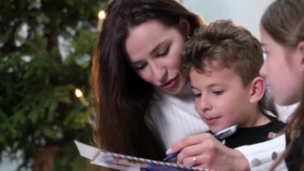 Ung mor med dotter och son nära julgranen — Stockvideo