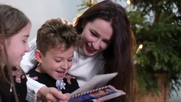 Mamãe e crianças lêem um livro, eles se divertem rindo juntos. — Vídeo de Stock