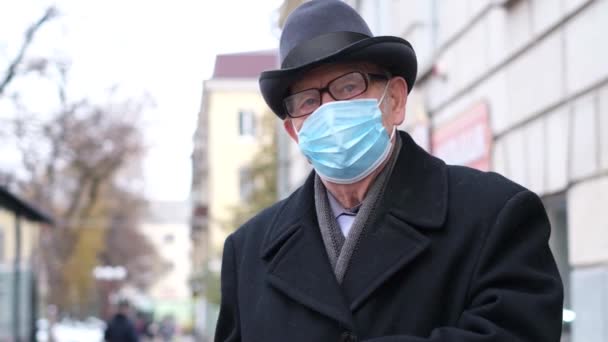 Egy védő maszkos nyugdíjas sétál a város utcáin.. — Stock videók