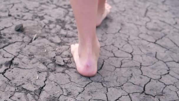Fille pieds nus marche sur la terre ferme du lac, sécheresse, fissures de la terre, pas d'eau. — Video