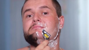 Genç adam banyoda tıraş köpüğü ve jiletle tıraş oluyor..