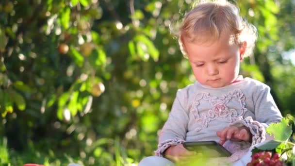 Bebé bonito segurando um smartphone e olhando para a tela na natureza. — Vídeo de Stock