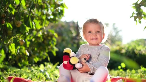 Malá veselá dívka hraje na trávě pod jabloní na dvorku za slunečného letního dne. — Stock video