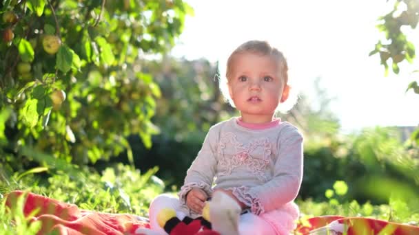 Söt liten flicka sitter i en grön trädgård leker.. — Stockvideo