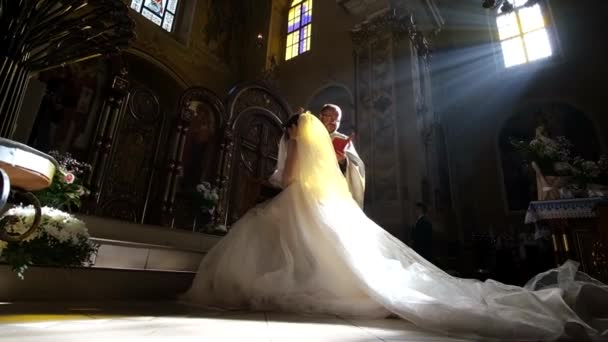 De bruid zweert bij God tegen de achtergrond van zonlicht in een prachtige christelijke kerk — Stockvideo