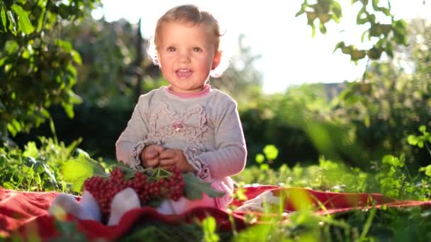 Lilla glada flicka på en solig sommardag sitter i trädgården och leker. — Stockvideo