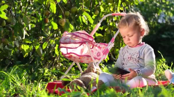 Rozkošné malé dítě, blondýnka, hrající si s medvídkem, sedící venku na zahradě. — Stock video