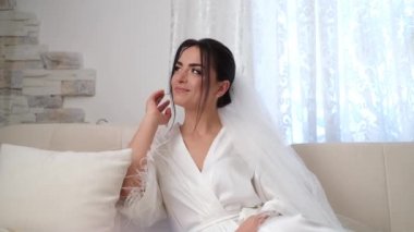 Esmer gelin düşünceli bir şekilde kanepede oturuyor ve başka tarafa bakıyor.. 