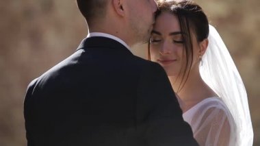 Gelin ve damat el ele tutuşuyor ve sarılıyorlar, çerçevede güzel bir güneş ışığı var.