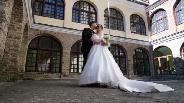 De bruid in een lange jurk knuffelt en kust de bruidegom, een date. Huwelijksdag — Stockvideo
