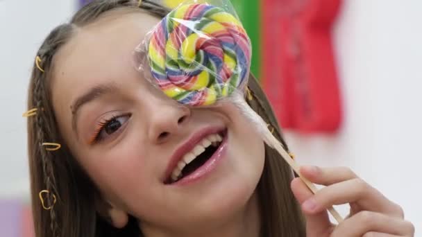 Schattig klein meisje met een kleurrijke lolly kijken naar de camera. — Stockvideo