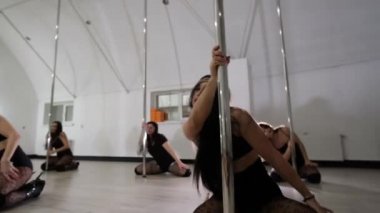 Bir grup genç kadın yüksek topuklularla sütunların yanında dans ediyor. Direk dansı