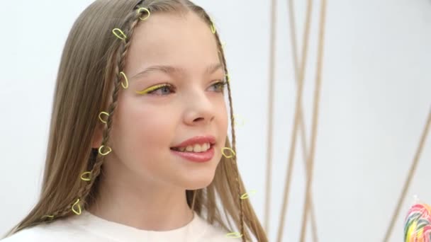Aranyos kislány színes nyalóka formájában szív pózol a kamera. — Stock videók