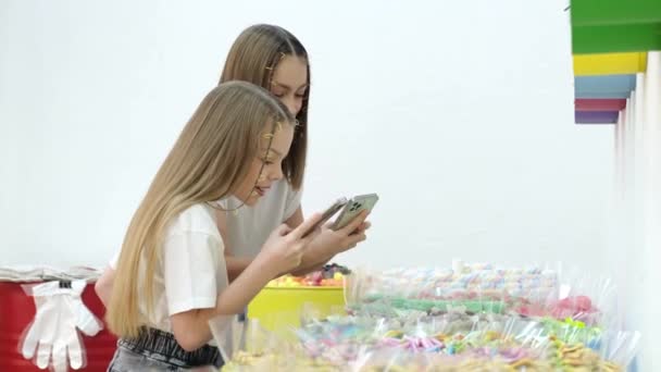 Twee kleine zusje meisjes in een snoepwinkel, ze zijn blij om snoep te fotograferen. — Stockvideo