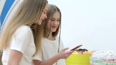 Mağazadaki iki kız arkadaş akıllı telefonlu şekerlerin fotoğraflarını çekiyor., 