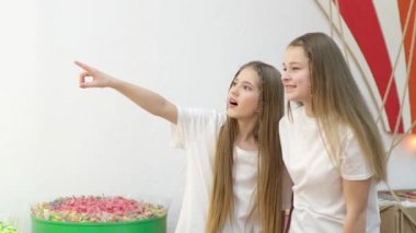 İki kız kardeş işaret parmaklarını vitrine doğrultuyor, gördüklerinden çok etkileniyorlar..