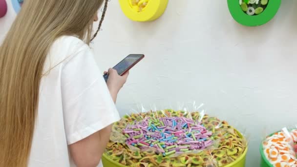 Teenage girl takes pictures of candy with a smartphone, she is in the store. — Stock Video