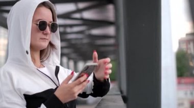 Şık bir genç kız akıllı telefon kullanıyor, güneş gözlüğü takıyor..