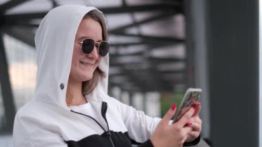 Güzel bir kız akıllı telefonunda bir mesaj okuduktan sonra gülümser ve bir cihaz kullanır.