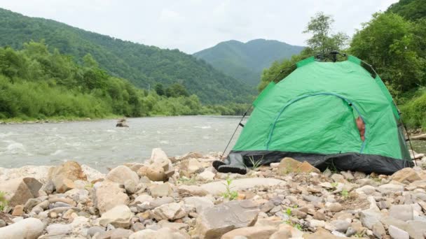 Самотній чоловік прокидається вранці в наметі, він провів ніч біля гірської річки . — стокове відео