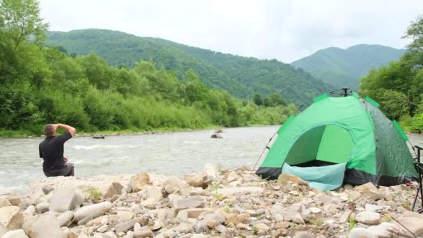 予算の観光客は、山の川で休憩、彼は夜のための緑のテントを設定します。. — ストック動画