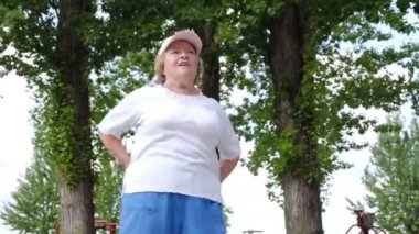 Emeklilik yaşında bir kadın parkta sabah sporu yaparken sırtını esnetir..