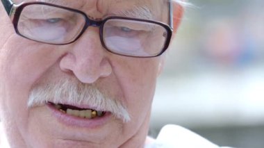 Gri bıyıklı ve gözlüklü yaşlı bir dede öfkeyle kameraya konuşuyor..