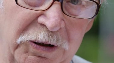 Gri saçlı büyükbaba kameraya konuşuyor, gözlük takıyor..