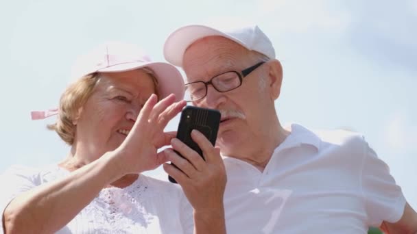 La nonna insegna al nonno a usare l'ultimo smartphone. Una famiglia di pensionati utilizza un gadget moderno — Video Stock