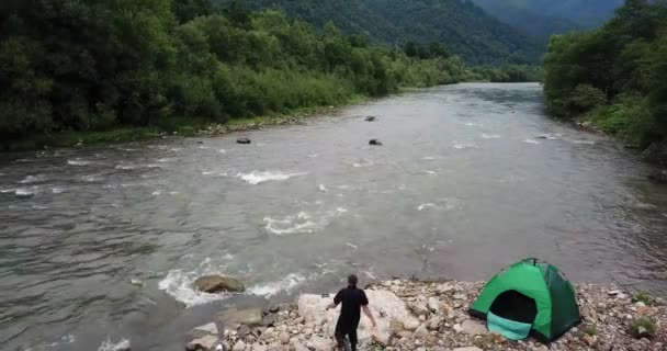 En fiskare fiskar genom att snurra, en utsikt över en bergsflod och ett grönt tält — Stockvideo