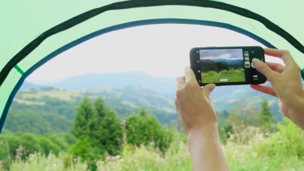 Dívka fotí s chytrým telefonem z hor ze svého stanu, v létě. — Stock video